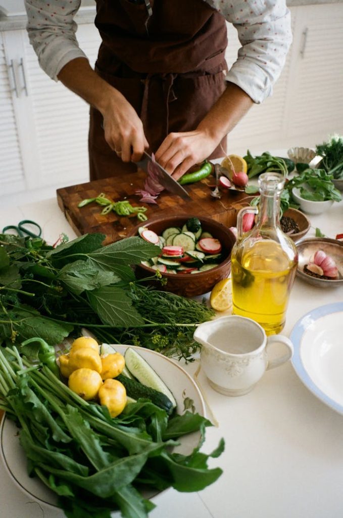 Adult preparing salad with fresh vegetables, knife, and olive oil in kitchen setting.